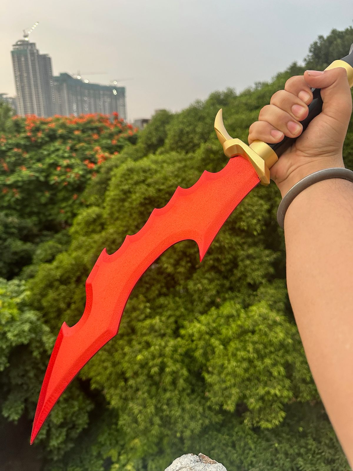 Red sword with gold handle held by a person against a green foliage background
