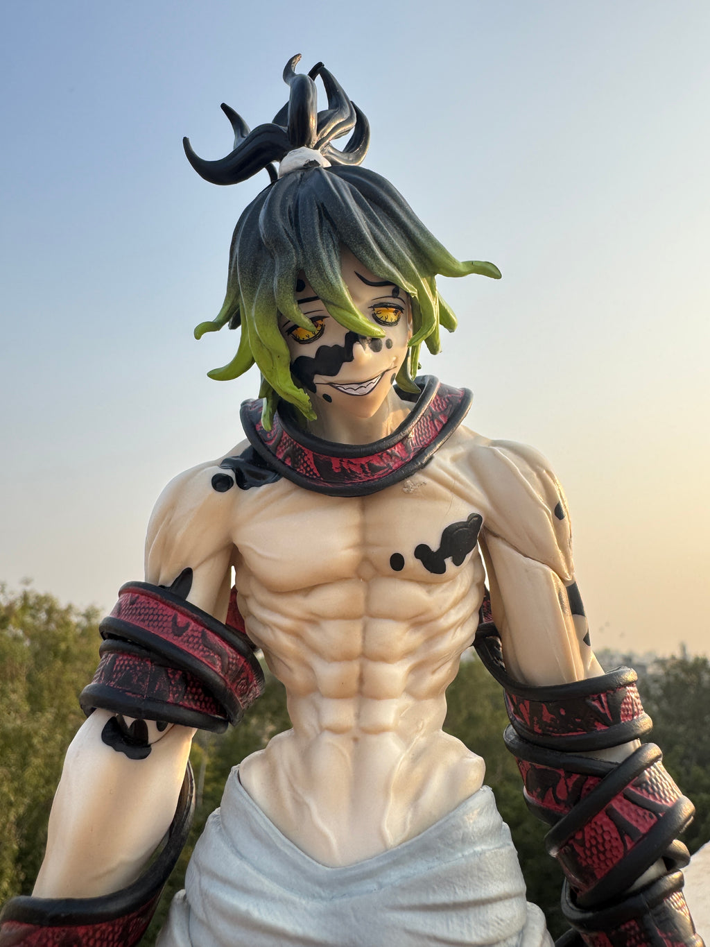 Statue of a character with green hair and red accents against a blurred natural background