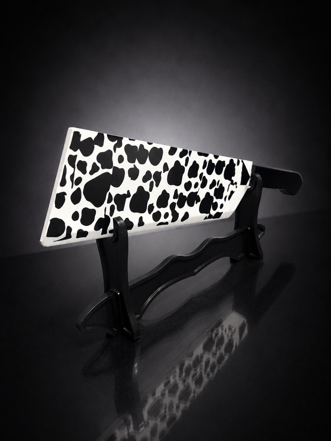 Angled view of cow pattern anime butcher blade replica with black handle on premium display stand for cosplay and collectors