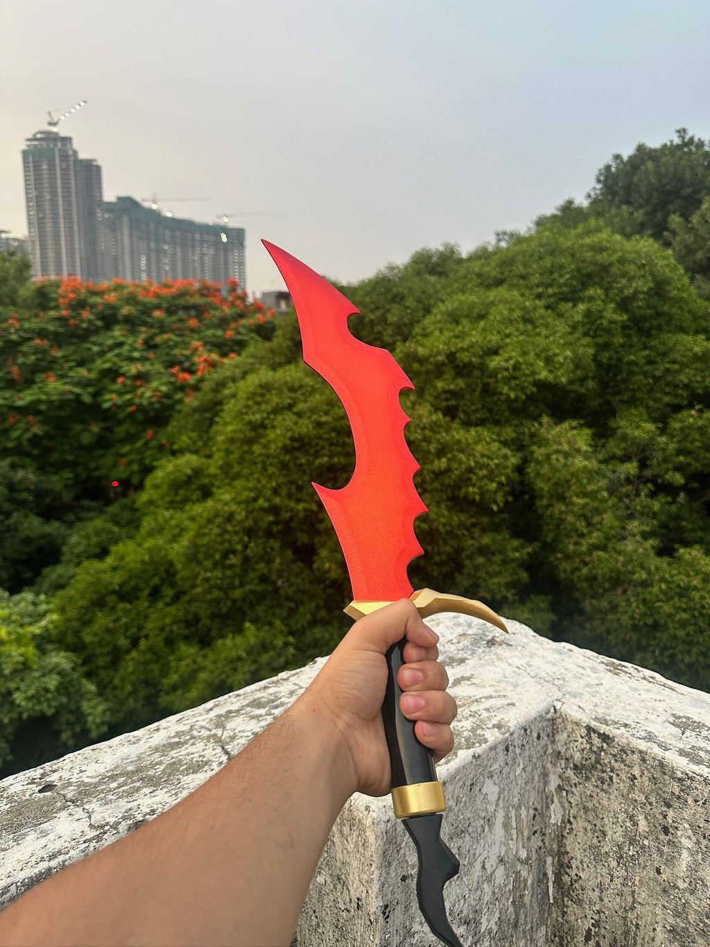 Red weapon held by a hand with a cityscape and trees in the background